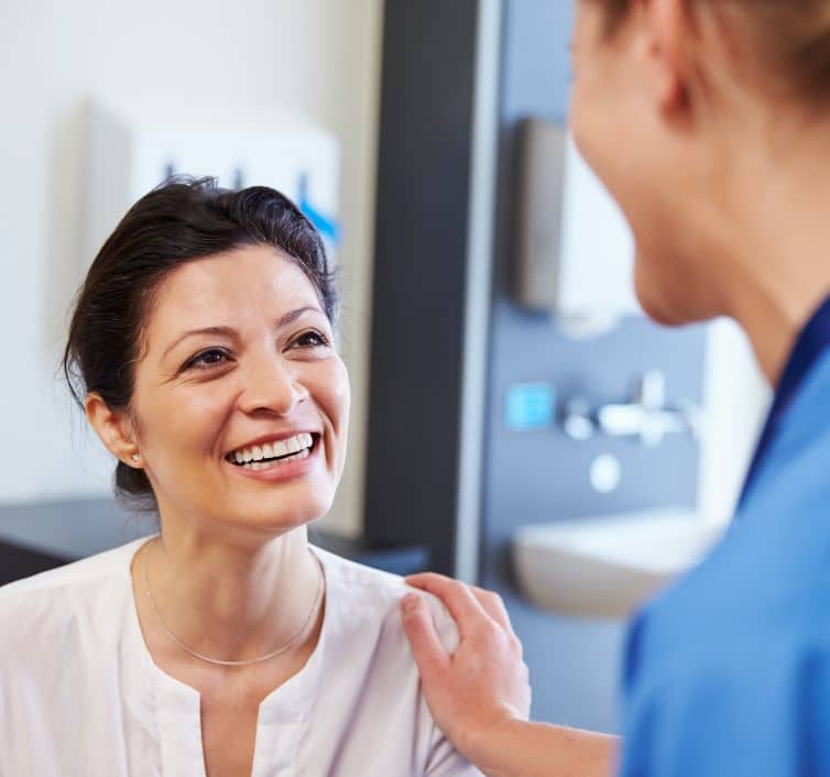 Image of a doctor holding up a mirror to the patient, the patient smiling and touching her nose